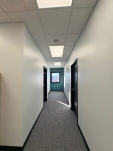 Completed commercial office corridor featuring drywall finishing, acoustical drop ceiling installation, LED lighting, and professional tenant improvement construction
